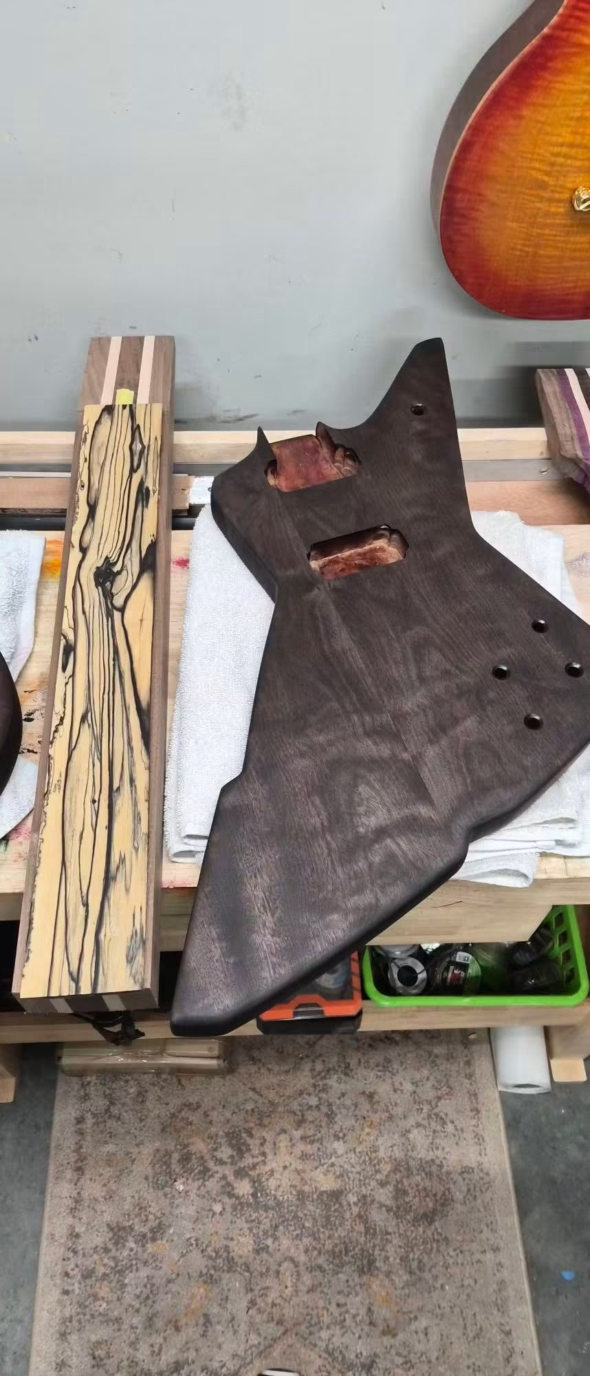 Angular guitar body with empty pickup cavities beside striped wood blanks