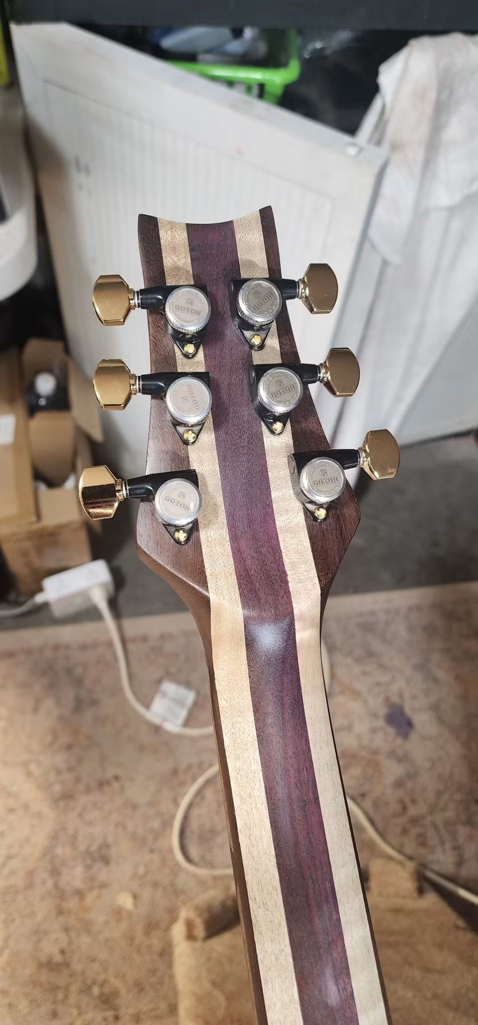 Back of a laminated guitar neck and headstock with gold tuners