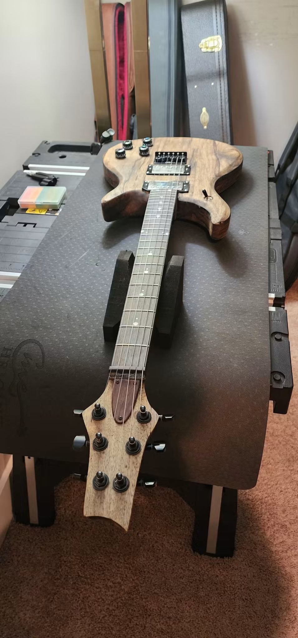 Assembled natural wood guitar resting on a padded workshop bench